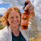 Claire Georges holding a bottle of Smoked Serrano Squash Reaper X hot sauce in a  farm field