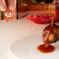 Person pouring Smoked Serrano Squash Reaper X hot sauce onto a chicken wing
