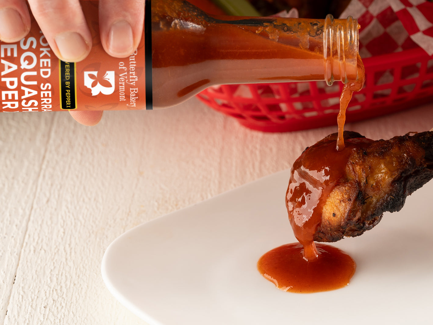 Person pouring Smoked Serrano Squash Reaper X hot sauce onto a chicken wing
