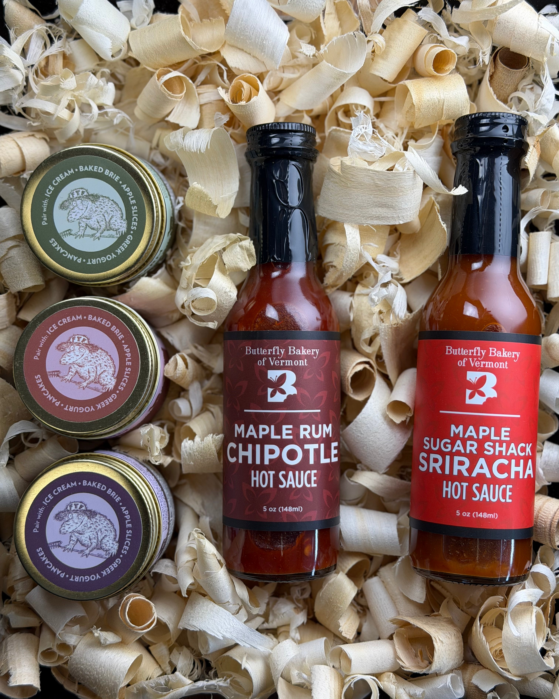 Two hot sauce bottles and three caramel jars in a box with wood shavings