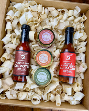 Two hot sauce bottles and three caramel jars in a box with wood shavings
