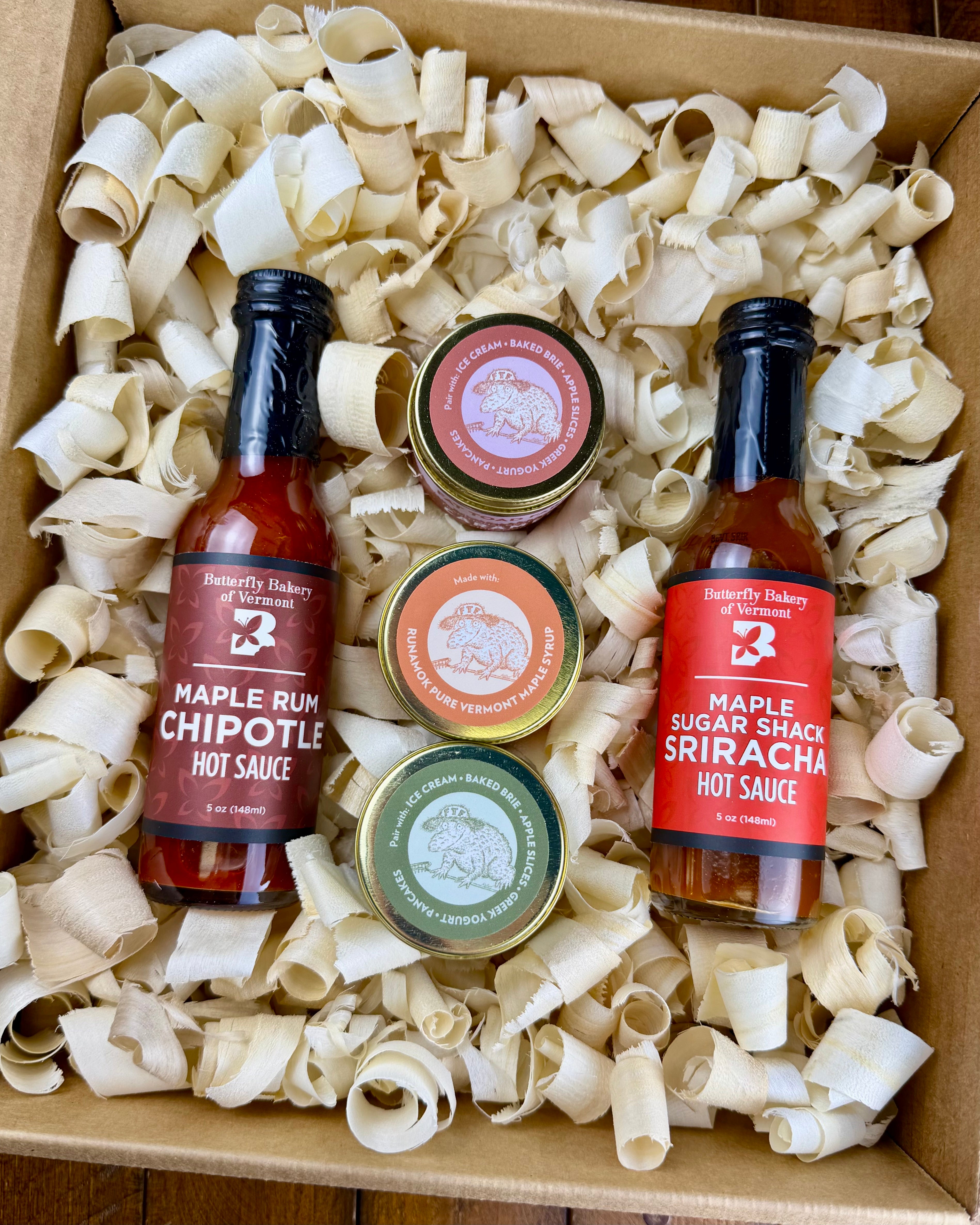 Two hot sauce bottles and three caramel jars in a box with wood shavings