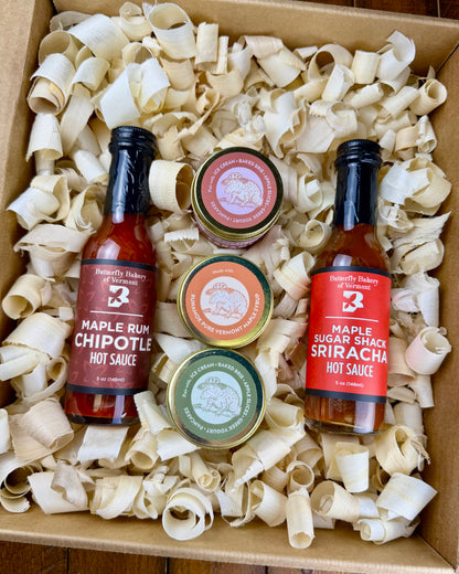 Two hot sauce bottles and three caramel jars in a box with wood shavings