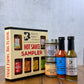 A Butterfly Bakery of Vermont hot sauce sampler box, along with 2 other bottles of hot sauce and 2 jars of mustard on a wood surface and gray background