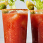Two glasses of Bloody Mary with spice powder on the rim and garnishes on a light background