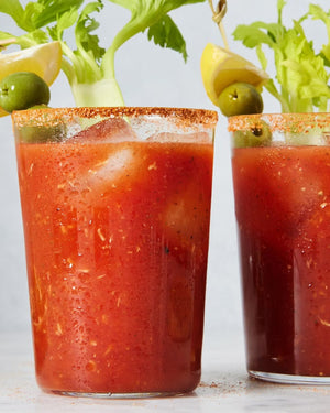 Two glasses of Bloody Mary with spice powder on the rim and garnishes on a light background