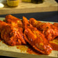 Spicy chicken wings smothered in hot sauce on a wooden board with a dark background