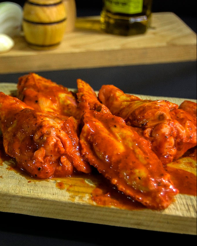 Spicy chicken wings smothered in hot sauce on a wooden board with a dark background