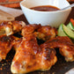Baked chicken wings with a side of hot sauce and vegetables on a wooden board.
