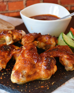 Baked chicken wings with a side of hot sauce and vegetables on a wooden board.