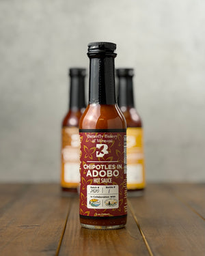 Bottle of Chipotles In Adobo hot sauce from Butterfly Bakery of Vermont on a wooden tabletop
