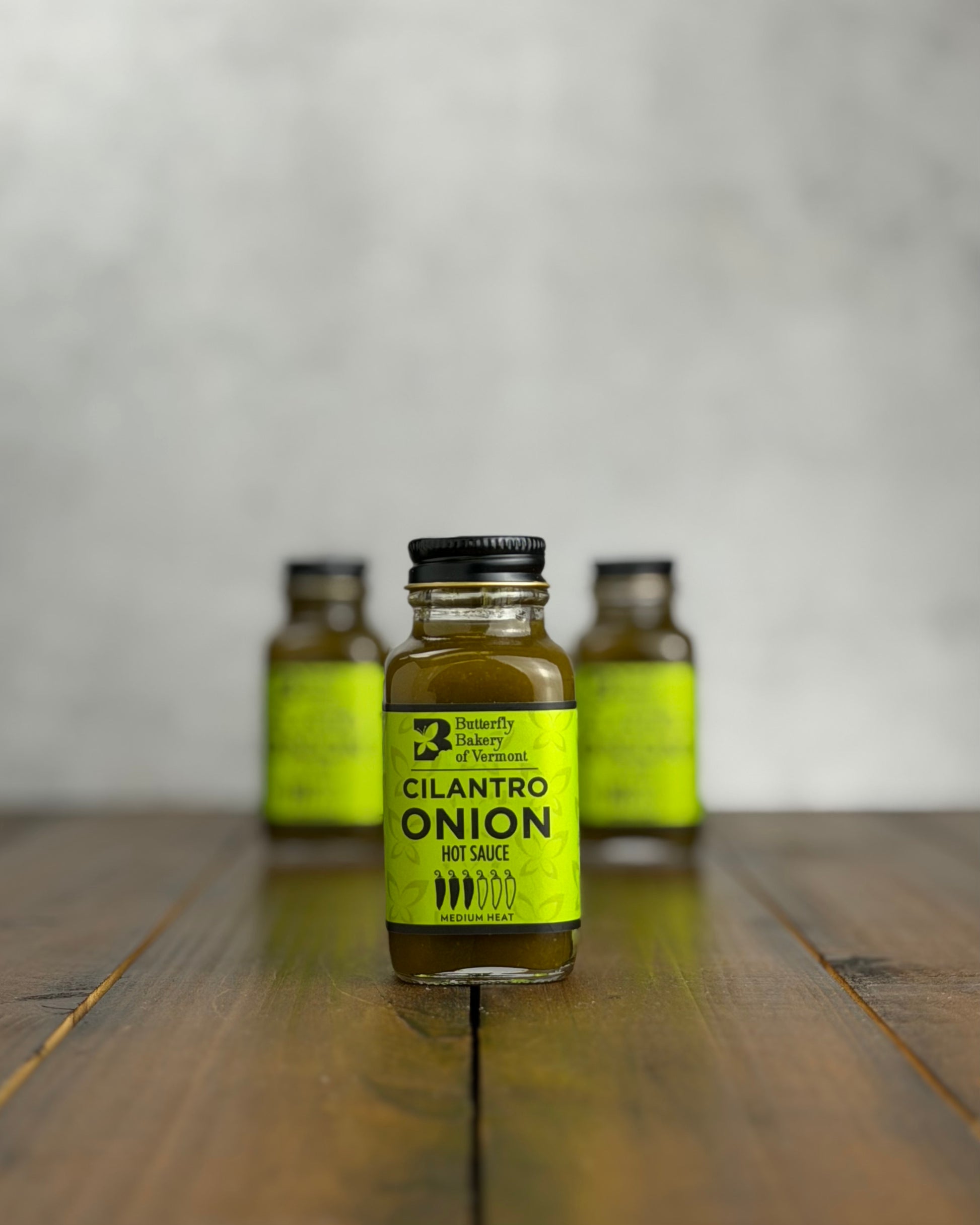 Bottle of Cilantro Onion hot sauce on a wooden surface with a gray background