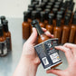 Person applying a label to a bottle of hot sauce with a blurred background of more bottles.