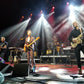 Guster performing on stage with bright lights and instruments.