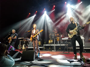 Guster performing on stage with bright lights and instruments.