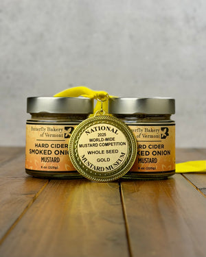 Two jars of Hard Cider Smoked Onion Mustard with a gold medal on a wooden surface.