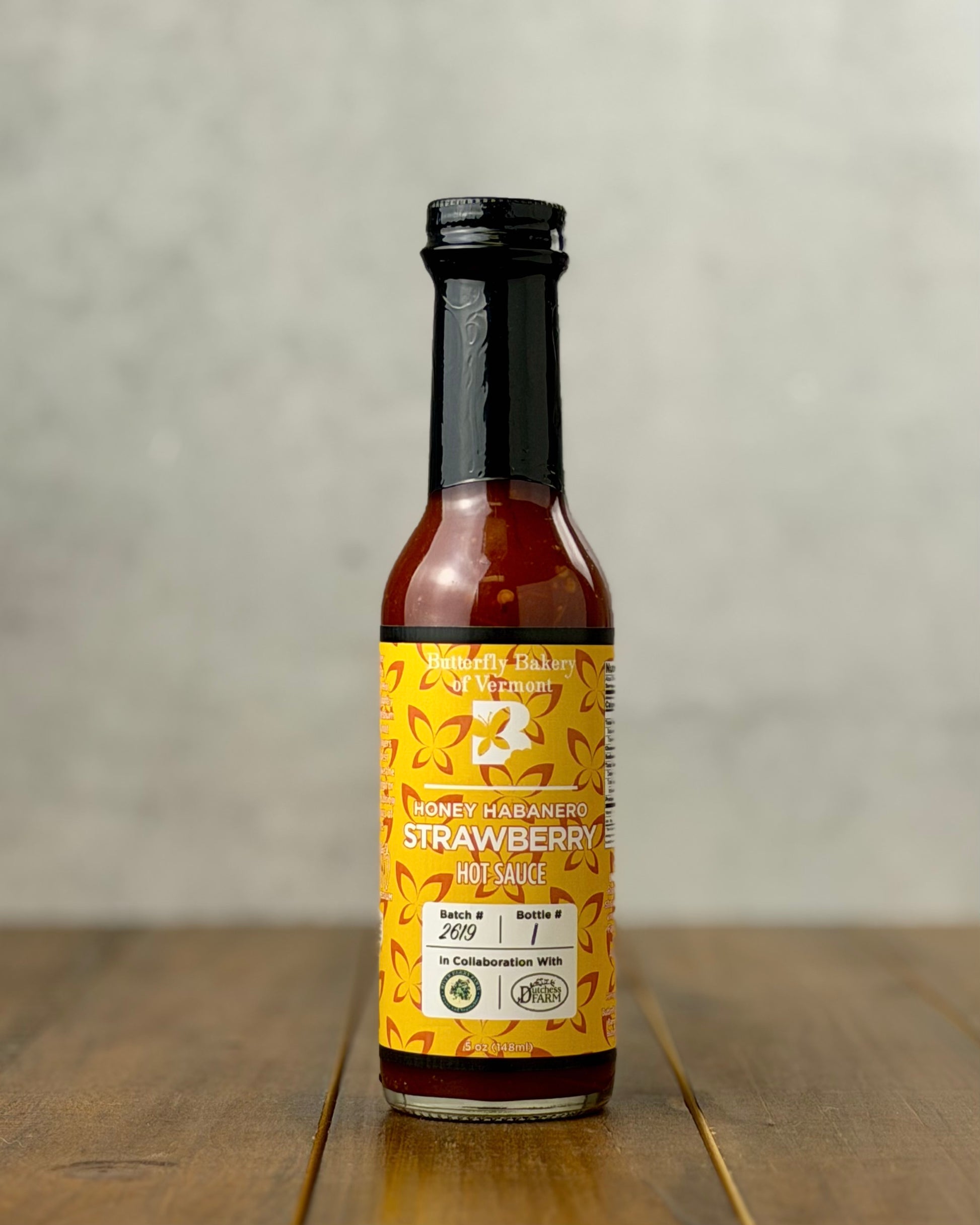 Bottle of Honey Habanero Strawberry hot sauce from Butterfly Bakery of Vermont on a wooden tabletop