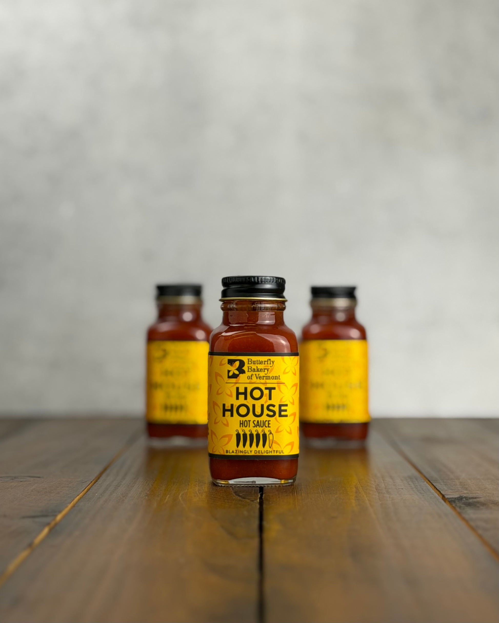 Three 2oz bottles of Hot House hot sauce on a wooden surface with a gray background