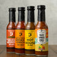 Bottles of all four hot sauces from Butterfly Bakery of Vermont that have appeared on Hot Ones, all on a wooden surface