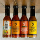 Bottles of all four hot sauces from Butterfly Bakery of Vermont that have appeared on Hot Ones, all on a wooden surface upside down