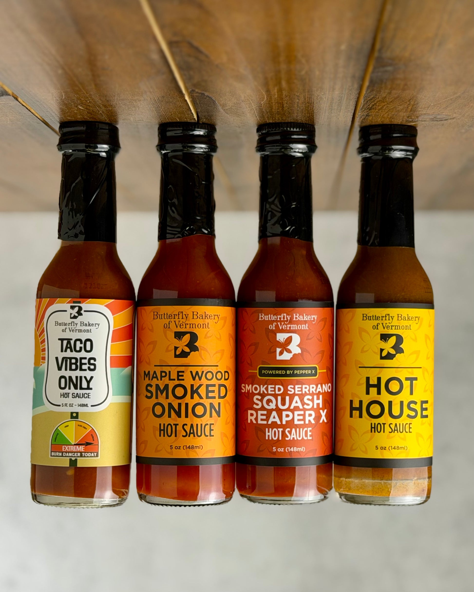 Bottles of all four hot sauces from Butterfly Bakery of Vermont that have appeared on Hot Ones, all on a wooden surface upside down