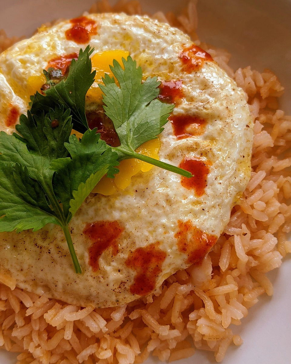 Fried egg on top of Spanish rice and topped with hot sauce and parsley