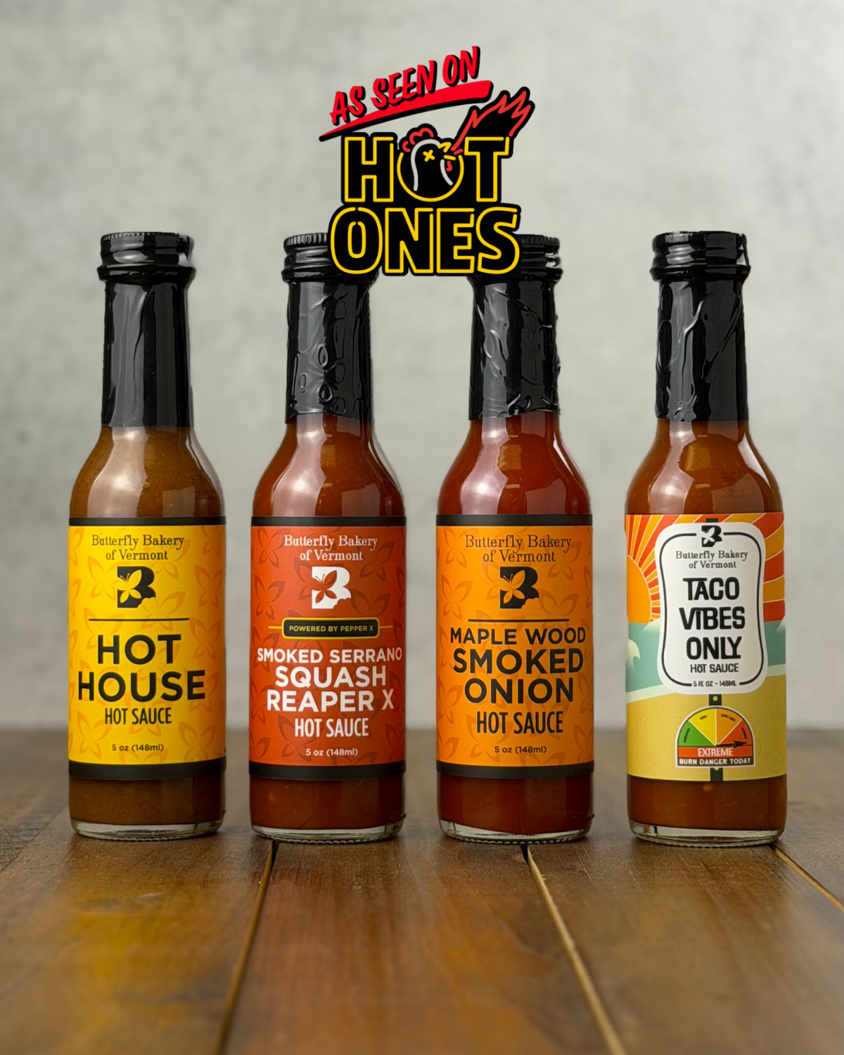 Four bottles of hot sauce with labels on a wooden surface, featuring 'Hot Ones' branding.