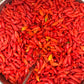 Large kettle filled with red ghost peppers and a stirring paddle.