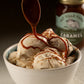 Bowl of ice cream being drizzled with caramel and a jar of caramel sauce in the background.