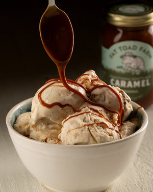 Bowl of ice cream being drizzled with caramel and a jar of caramel sauce in the background.