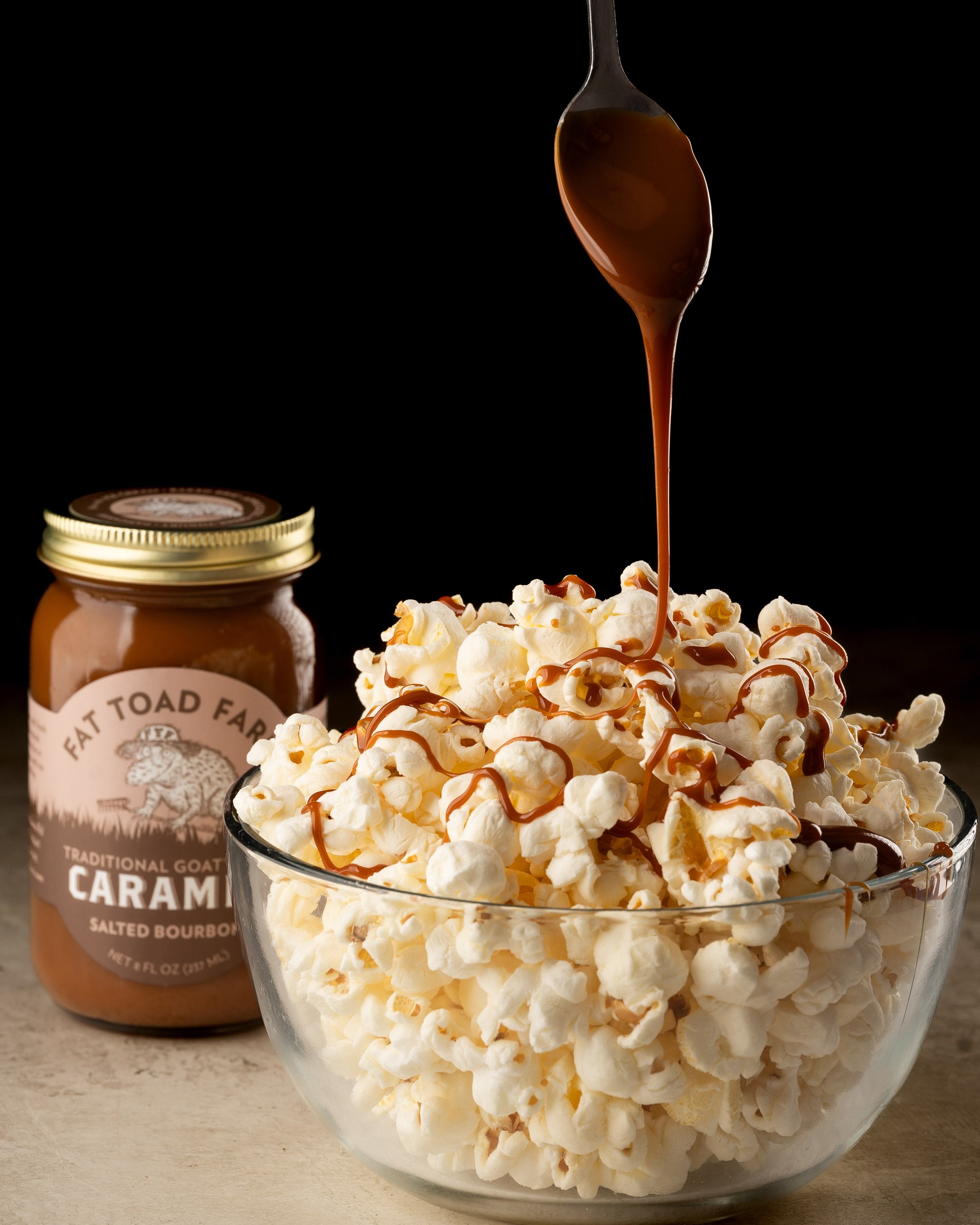 Bowl of popcorn with caramel being drizzled over it, next to a jar of caramel sauce.
