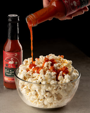Hot sauce being poured onto popcorn with a bottle of Ooh La La hot sauce in the background.