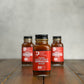 2oz bottle of Maple Sugar Shack Sriracha Hot Sauce with decorative elements on a wooden surface