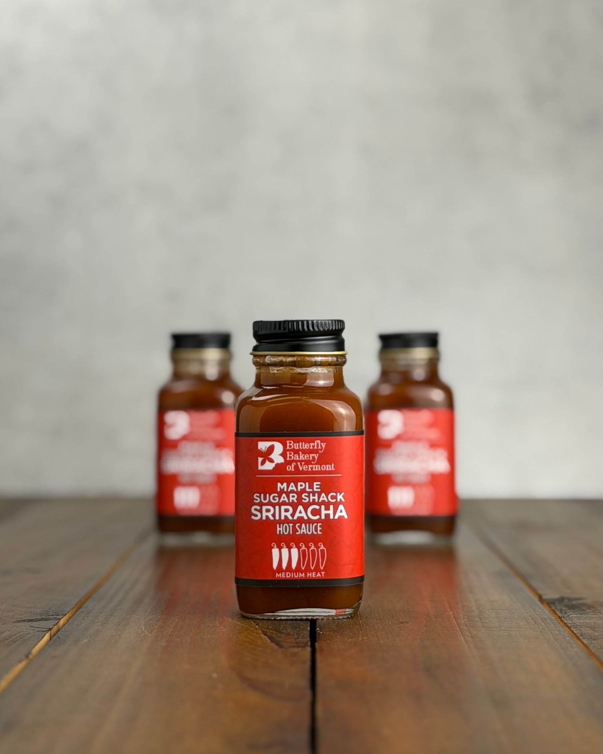 2oz bottle of Maple Sugar Shack Sriracha Hot Sauce with decorative elements on a wooden surface