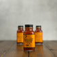 2oz bottle of Maple Wood Smoked Onion Hot Sauce on a wooden surface with a gray background