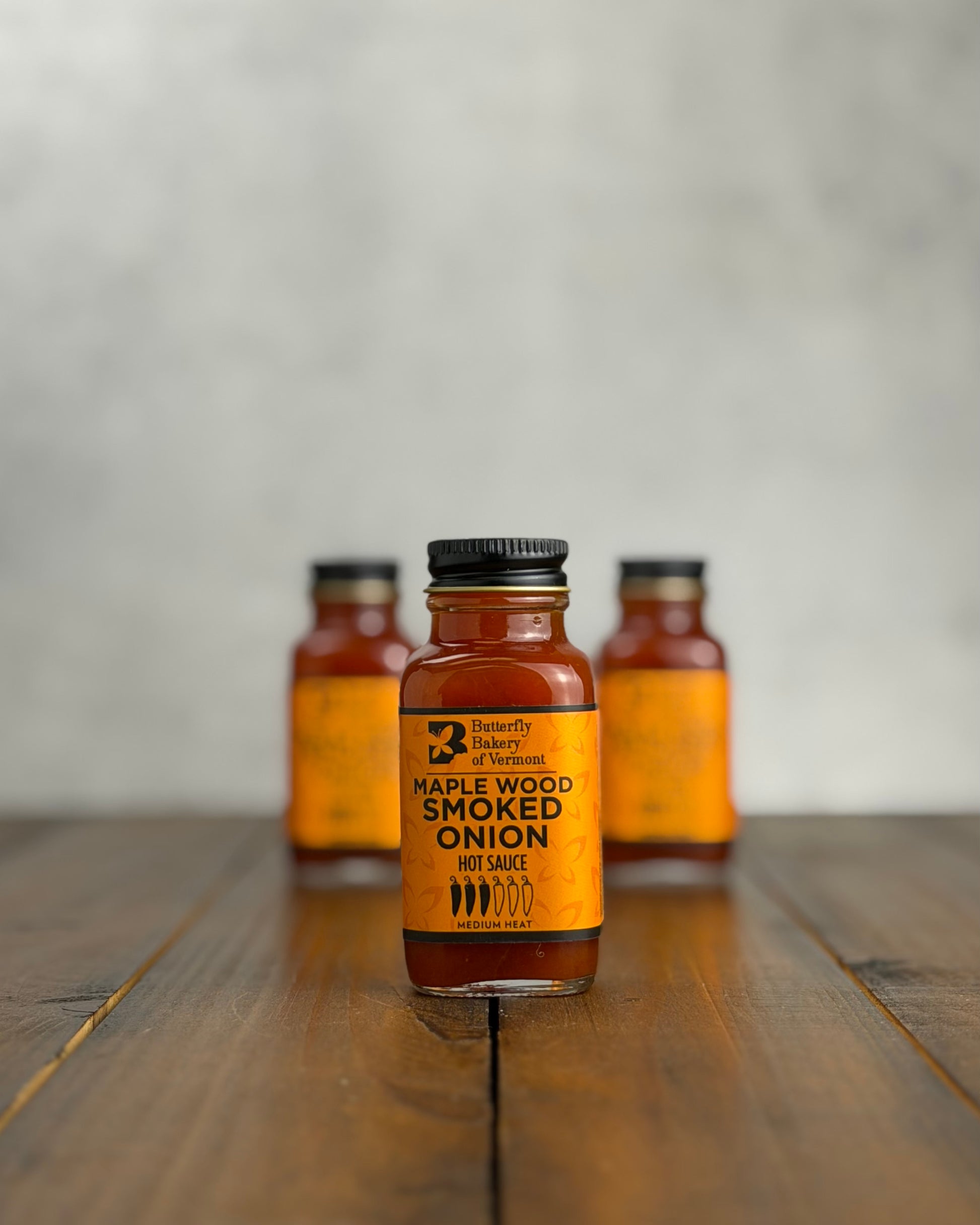2oz bottle of Maple Wood Smoked Onion Hot Sauce on a wooden surface with a gray background