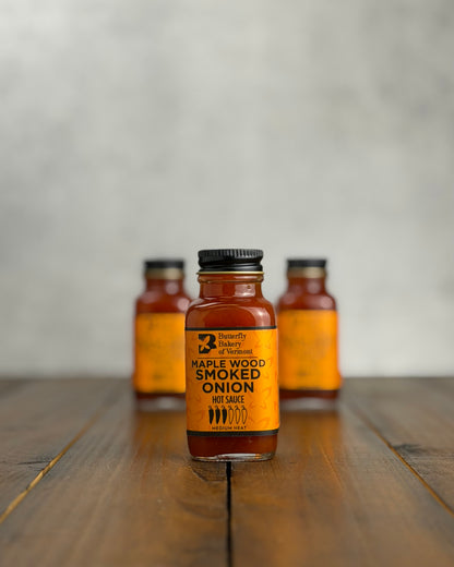 2oz bottle of Maple Wood Smoked Onion Hot Sauce on a wooden surface with a gray background