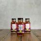 Three 2oz bottles of 'Mellow Vibes Only' sauce on a wooden surface with a gray background
