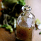 Glass bottle of salad dressing on a wooden surface with blurred salad in the background