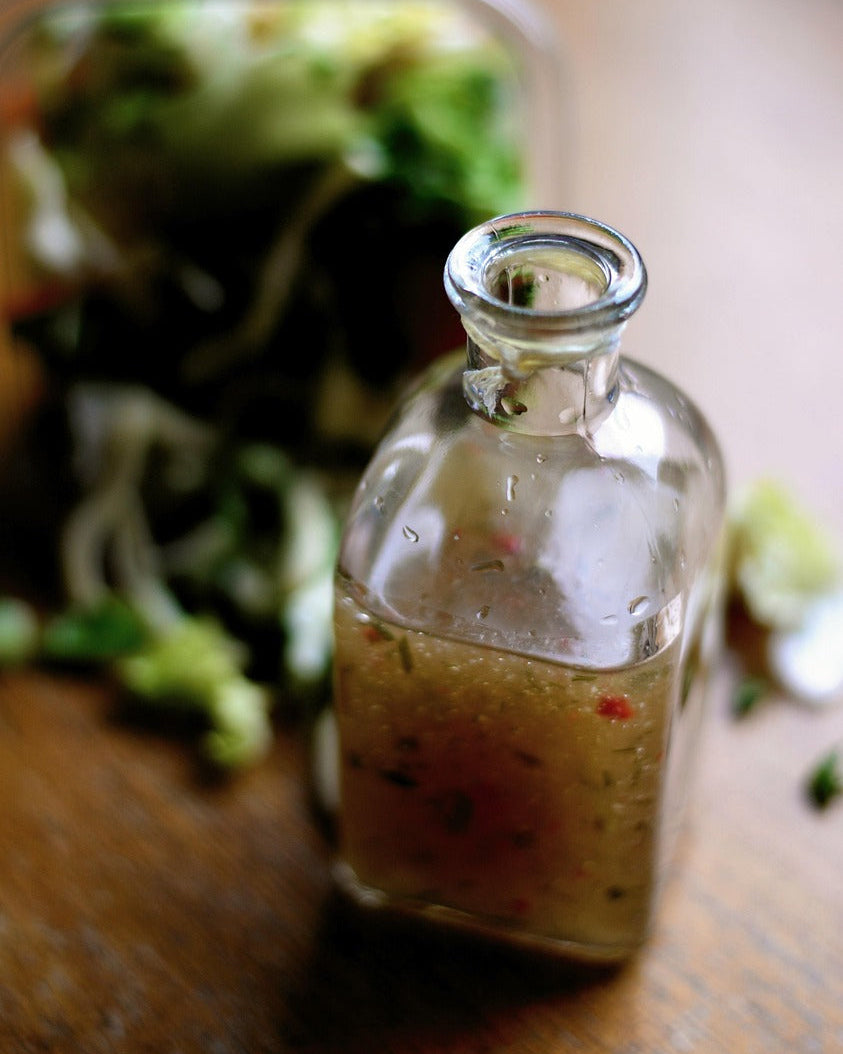 Glass bottle of salad dressing on a wooden surface with blurred salad in the background