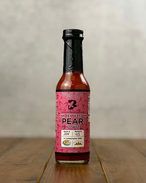 Bottle of Pink Peppercorn Pear hot sauce from Butterfly Bakery of Vermont on a wooden tabletop