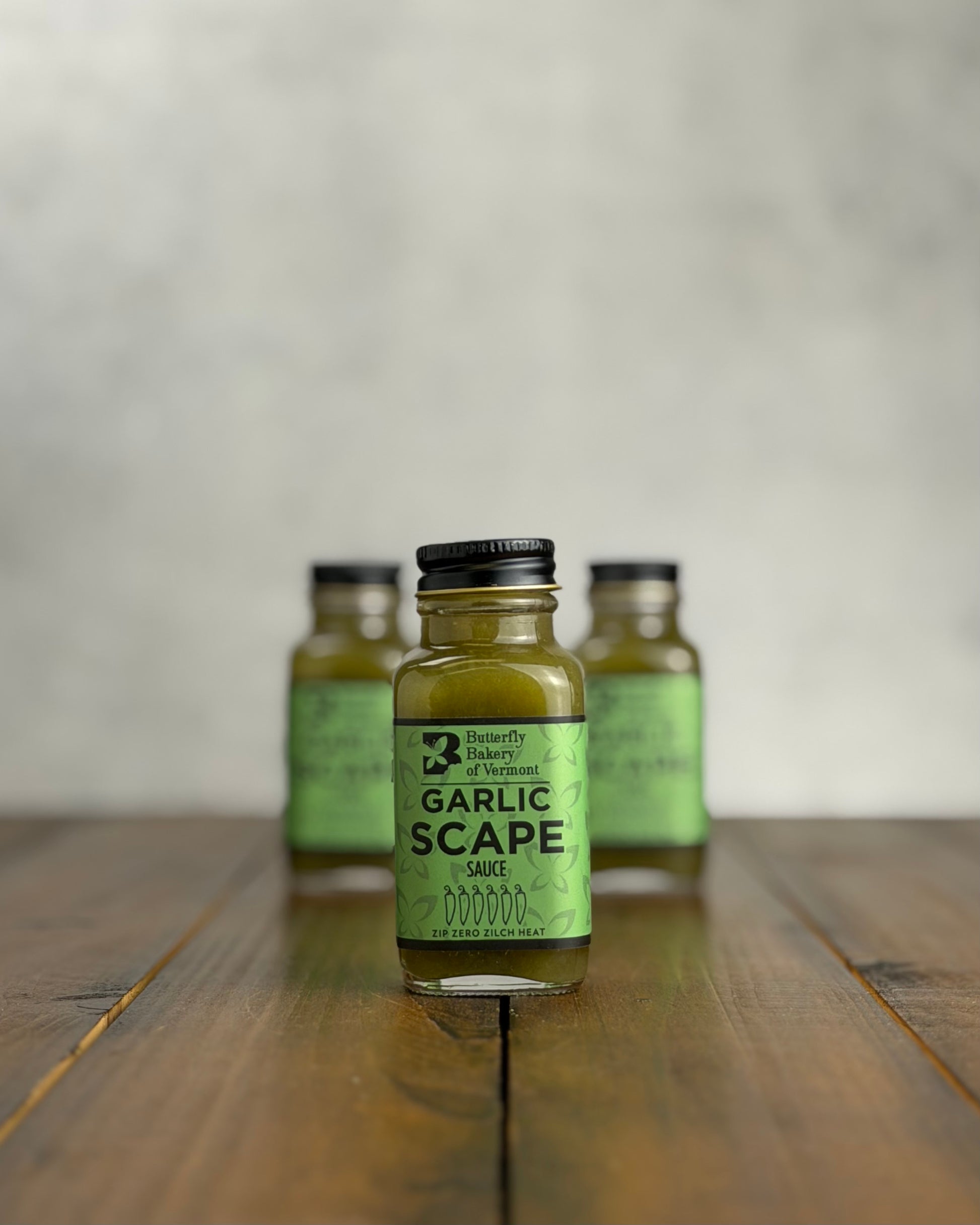 2oz bottle of Garlic Scape Sauce on a wooden surface with a neutral background