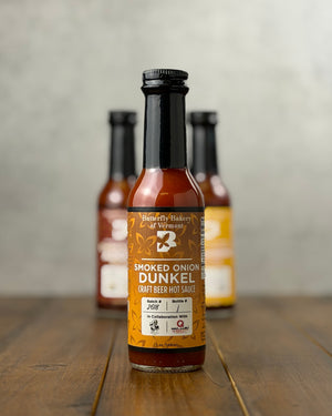 Bottle of Smoked Onion Dunkel Craft Beer hot sauce from Butterfly Bakery of Vermont on a wooden tabletop