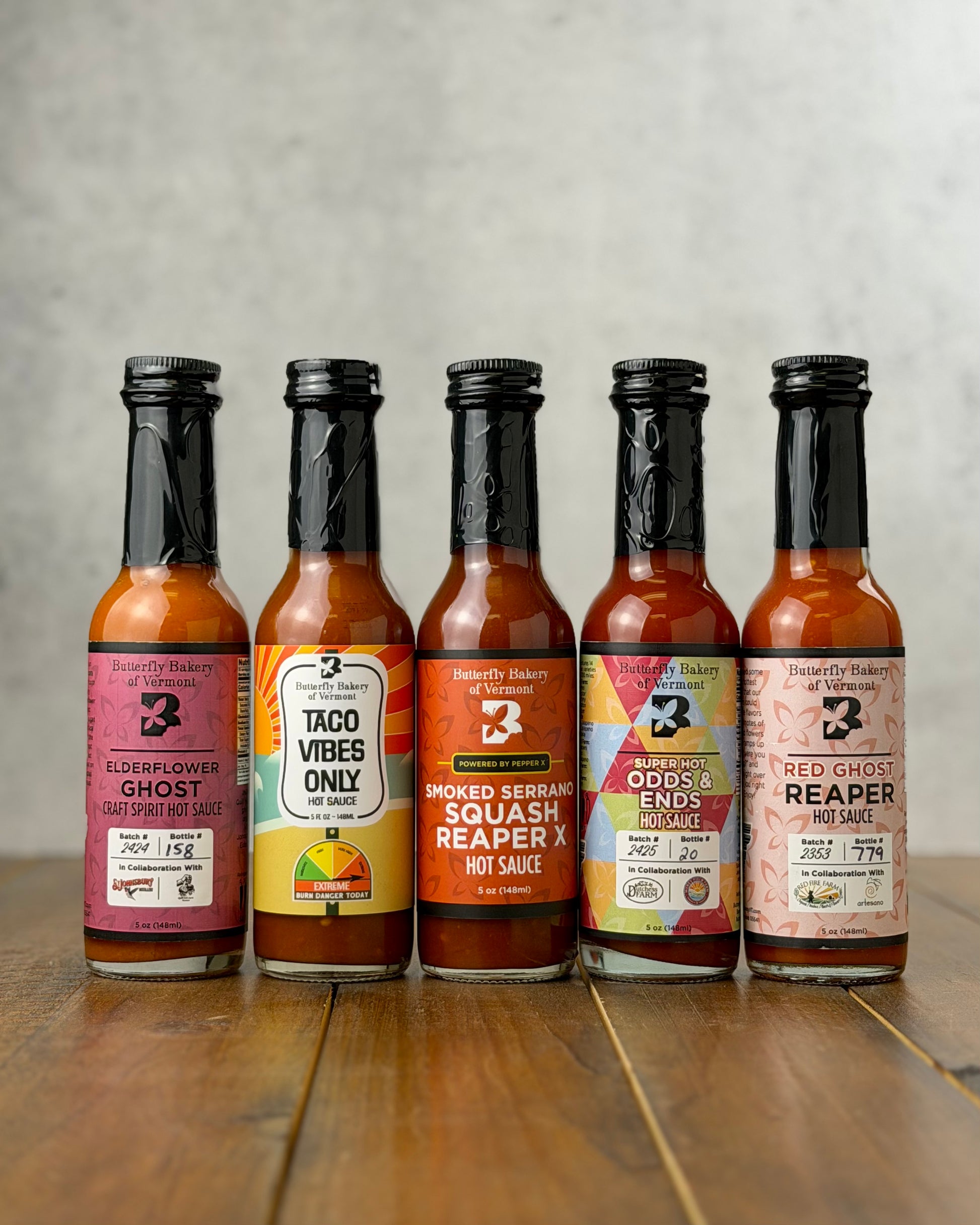 Butterfly Bakery of Vermont's 5 hottest hot sauces lined up on a wood surface and a gray background