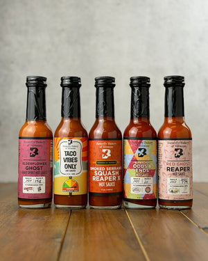 Butterfly Bakery of Vermont's 5 hottest hot sauces lined up on a wood surface and a gray background