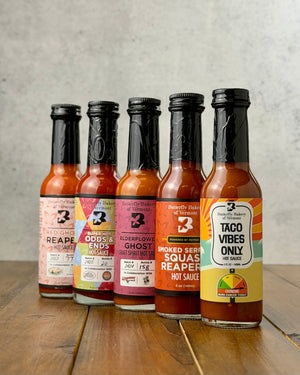 Butterfly Bakery of Vermont's 5 hottest hot sauces lined up on a wood surface and a gray background