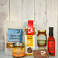 Assorted Butterfly Bakery of Vermont products including hot sauce, mustard, granola and Fat Toad Farm caramel on a stone surface with a gray background.