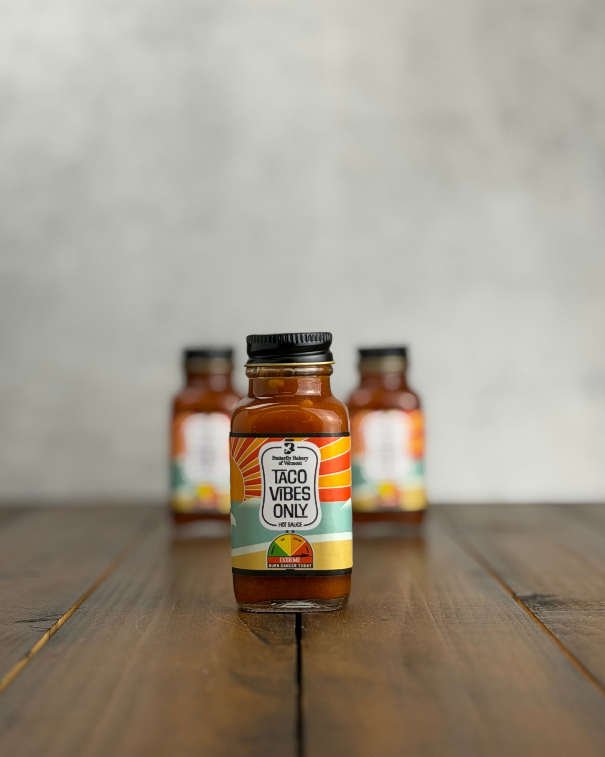 2oz bottle of 'Taco Vibes Only' sauce on a wooden surface with a gray background