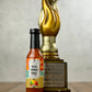 Bottle of 'Taco Vibes Only' hot sauce with a gold trophy on a wooden surface.