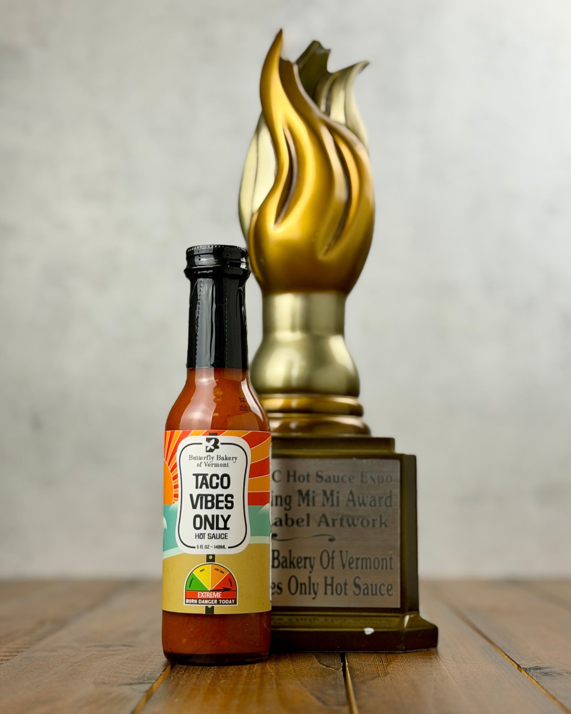 Bottle of 'Taco Vibes Only' hot sauce with a gold trophy on a wooden surface.